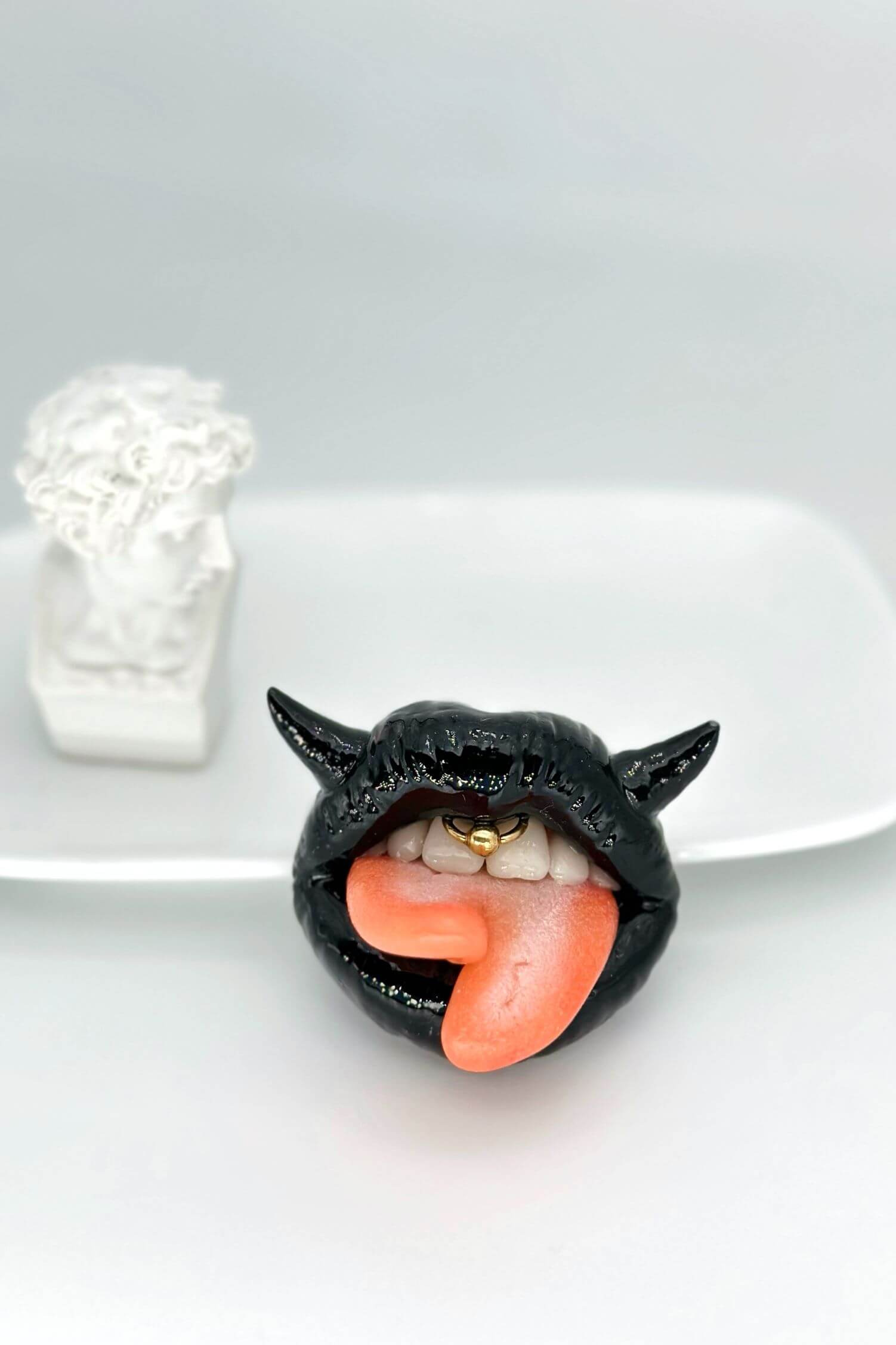 Handmade polymer clay black lips with split tongue, horns, and smile piercing, a unique and eye-catching wearable art by ioArtStudio